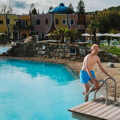 Junger blonder Mann steigt ins Thermalbecken im Rogner Bad Blumau